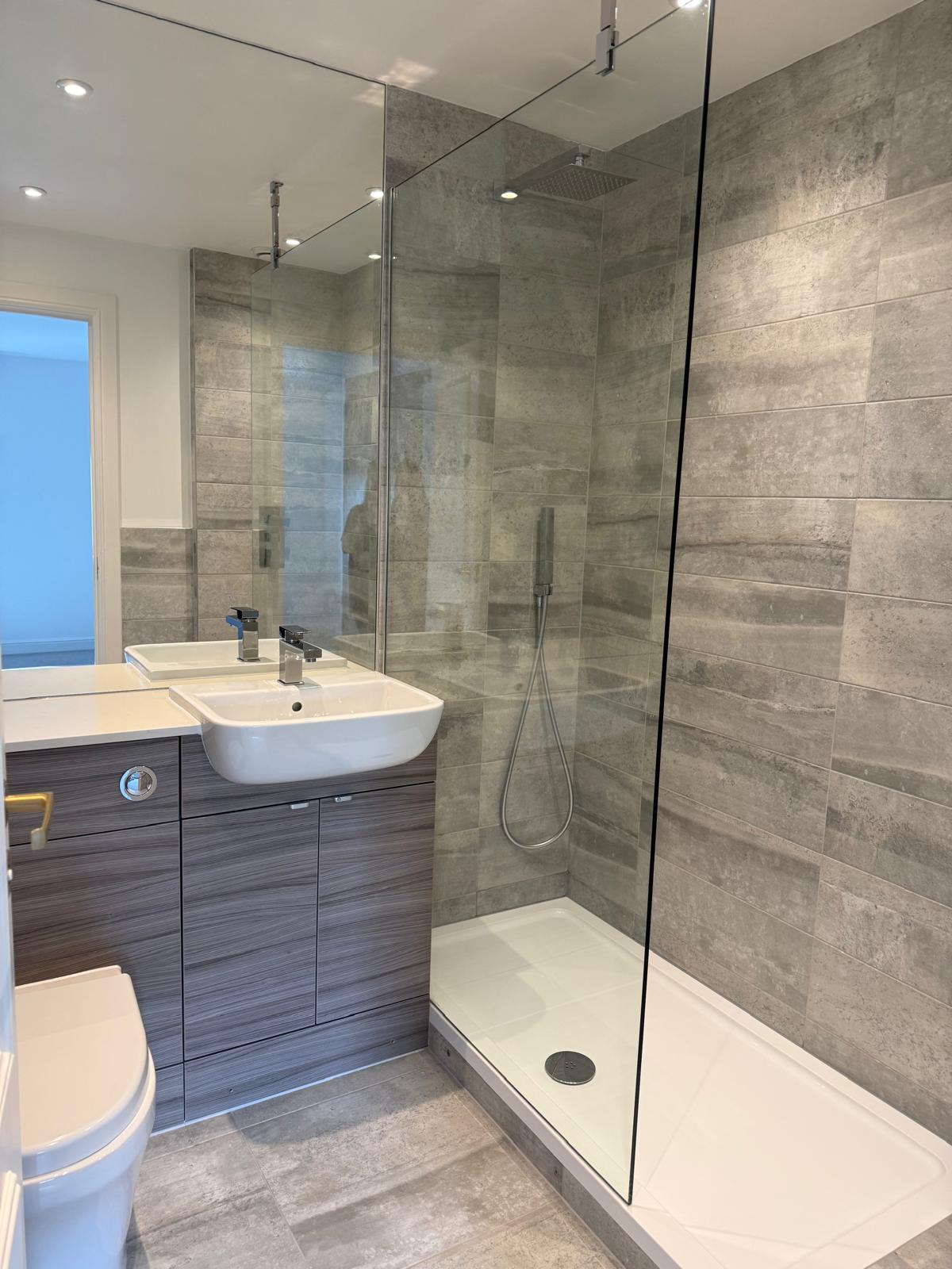 Stone-effect tiled shower room with a glass walk-in screen, basin vanity unit and WC, cleaned and polished