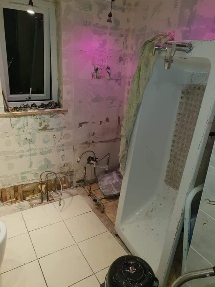 Bathroom mid strip-out with the old bath removed and set aside and the feed pipework capped off