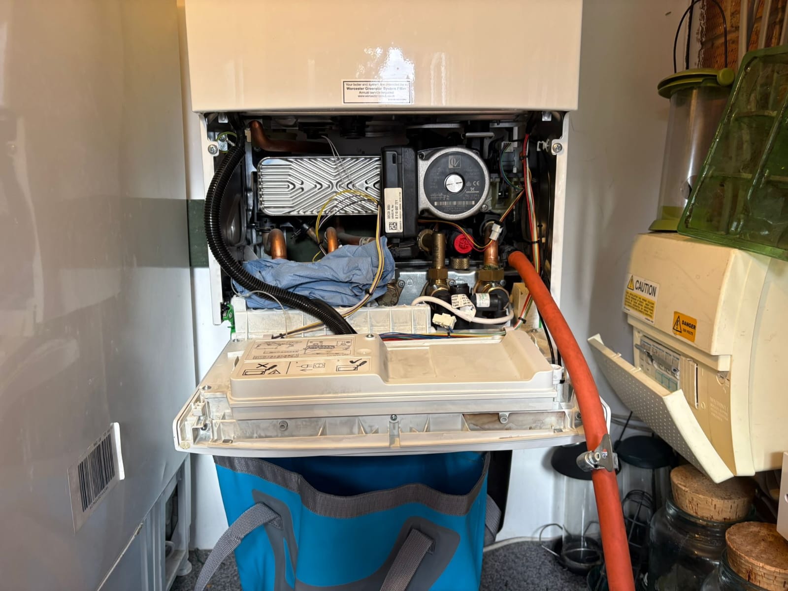 Wall-mounted Worcester combi boiler with the front cover removed, exposing the pump, heat exchanger and internal pipework during a service