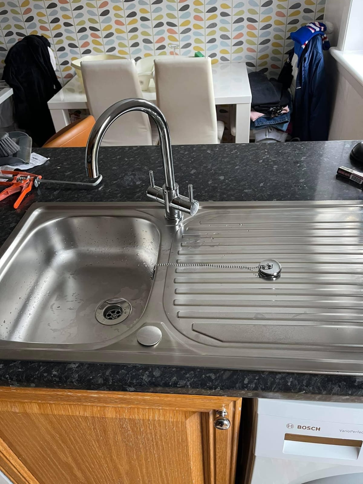 Chrome swan-neck mixer tap fitted to a stainless steel kitchen sink and drainer in a granite worktop
