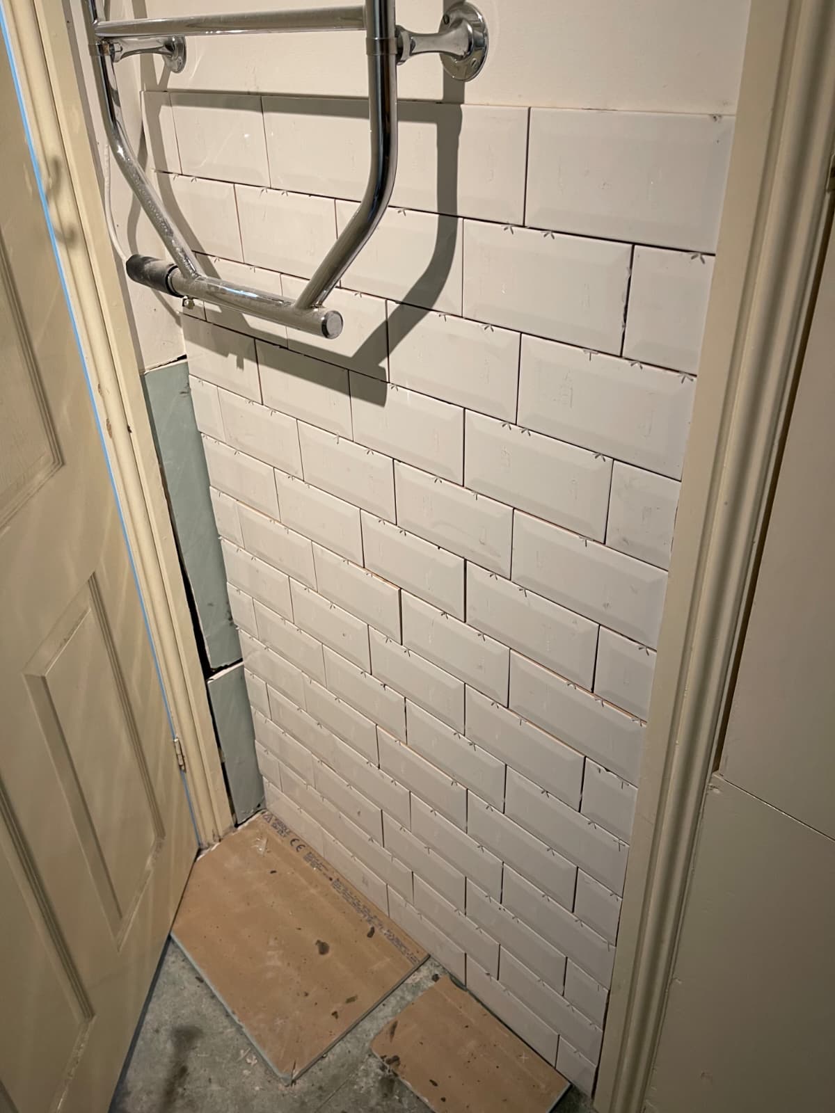 Shower recess freshly tiled in white metro tiles with spacers still in place, alongside chrome pipework