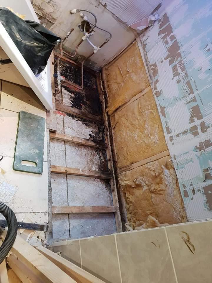Bathroom wall stripped back to the studwork and insulation, exposing old pipework ready for replacement
